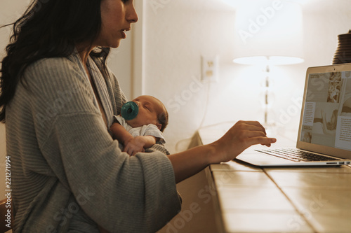 Картината върху платно Mother using a computer and holding her baby
