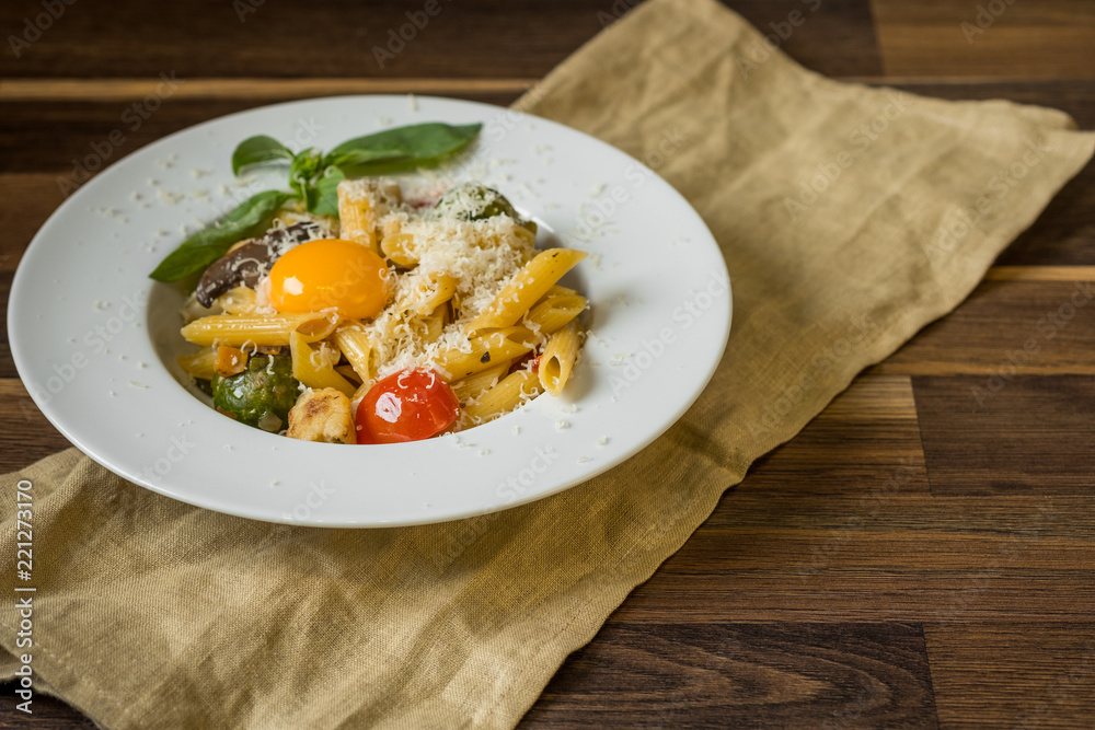 Italian pasta with cheese, vegetables and egg yolk served portion on wooden background.