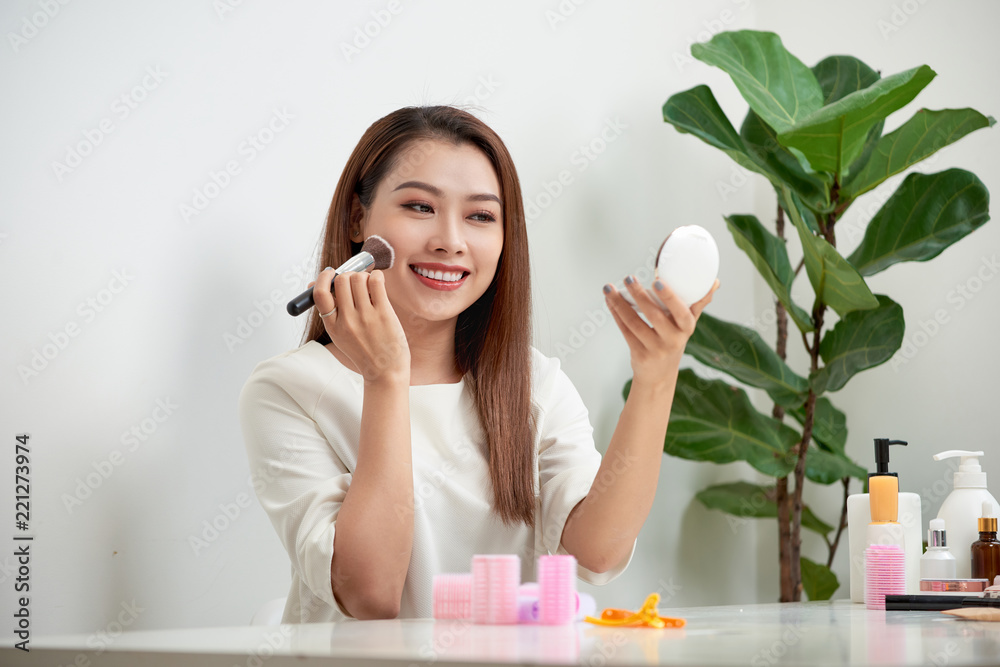 young beautiful woman applying her make-up with a big brush , looking in a mirror young beautiful woman applying her make-up with a big brush , looking in a mirror