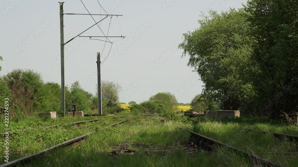 Wide shot of forgotten and abandoned railway line train tracks overgrown with grass and weeds during summer in England Wide shot of forgotten and abandoned railway line train tracks overgrown with grass and weeds during summer in England