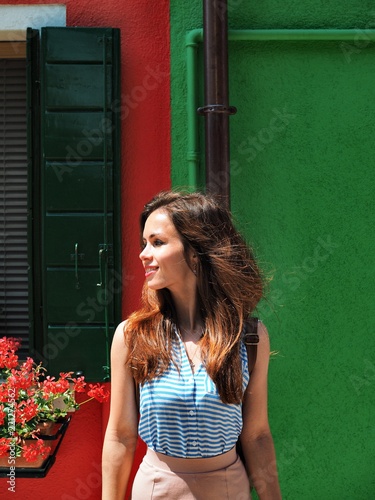 Portrait of brunette girl with long hair on the background of bright red and green wall of the house in Venice, girl winks, squinted one eye