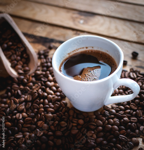 Close-up of black coffee in white cup  with coffee beans on wooden background