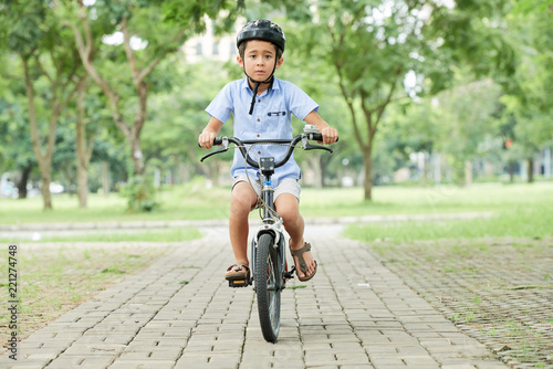 Fototapeta Naklejka Na Ścianę i Meble -  LIttle Vietnamese boy wearing helmet when cycling in summer park