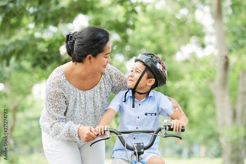 Mother helping her little son cycling in park