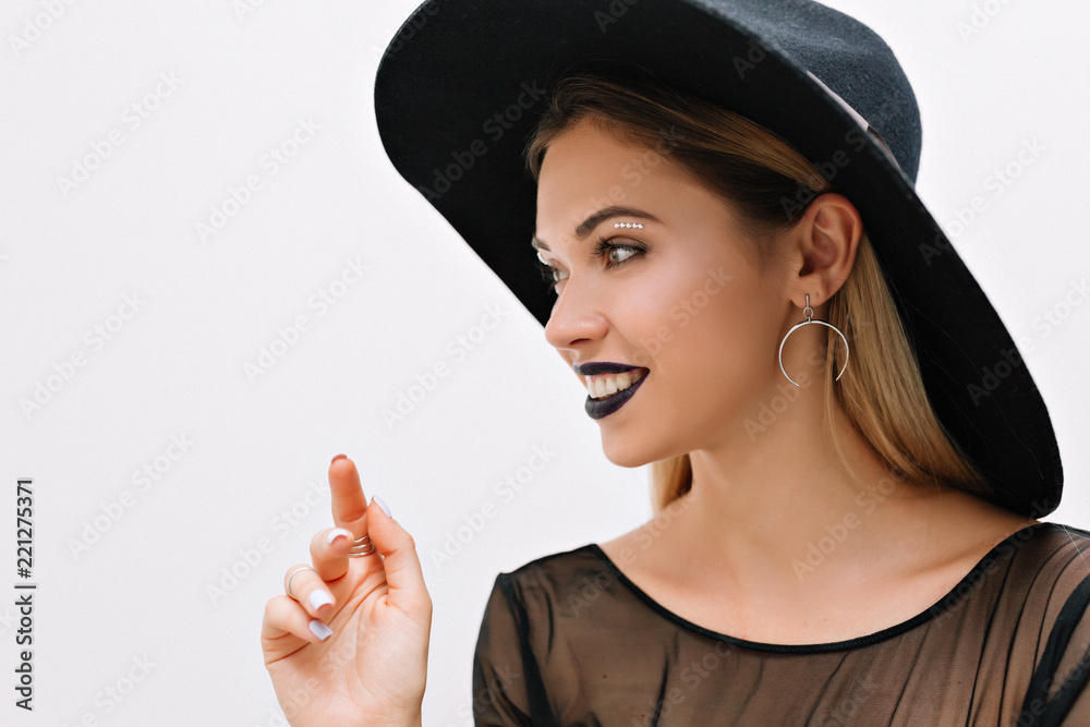 Close up indoor profile portrait of smiling happy charming woman prepearing for carnaval halloween party wearing black hat with brightful make up over isolated background Close up indoor profile portrait of smiling happy charming woman prepearing for carnaval halloween party wearing black hat with brightful make up over isolated background