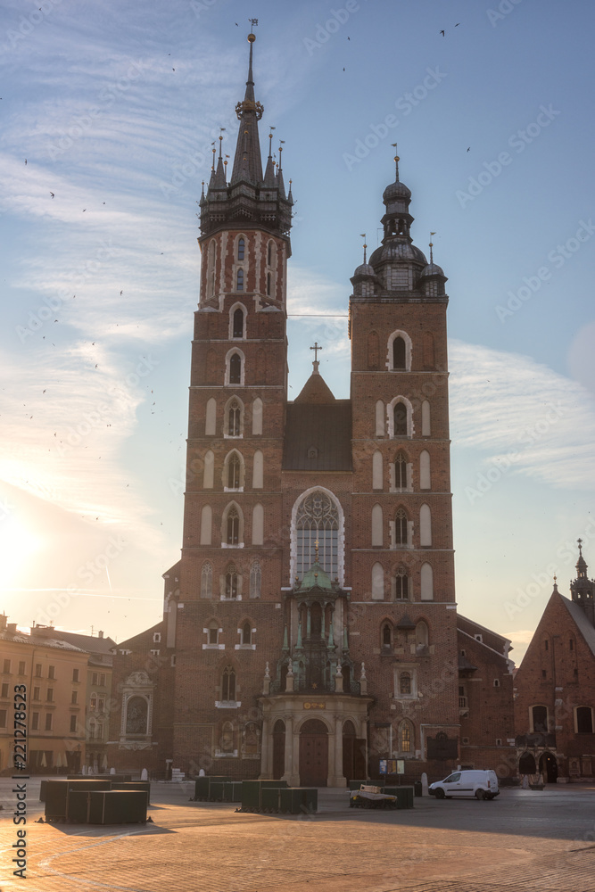 St. Mary's Basilica (Church of Our Lady Assumed into Heaven) on the Main Market square in Krakow at sunrise, vertical image with blue sky, sun and flying birds, Poland, Europe