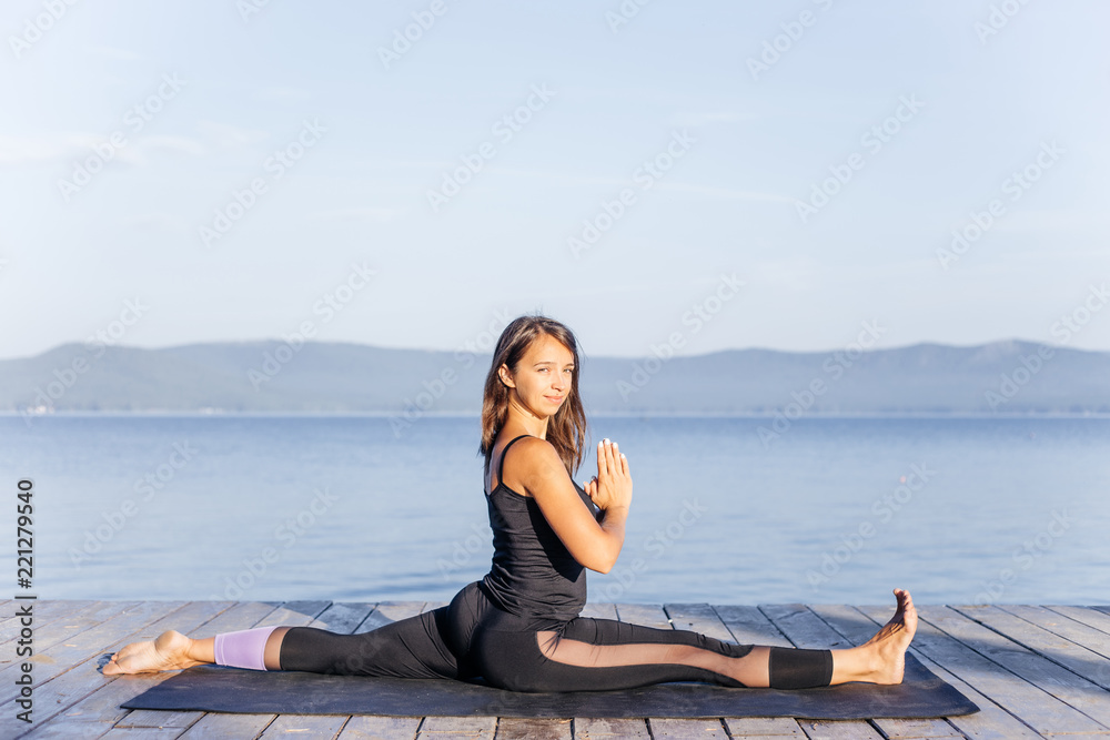 Young attractive smiling woman practicing yoga on a lake
