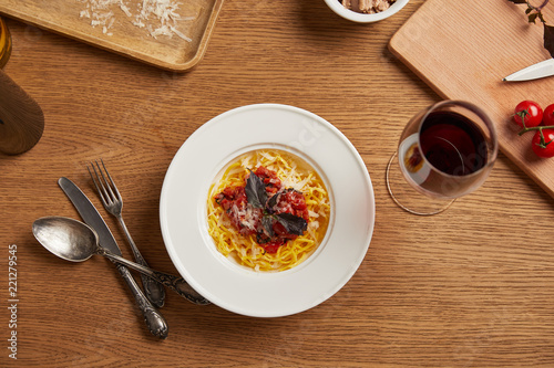 top view of plate of pasta with various ingredients and wine around on wooden table