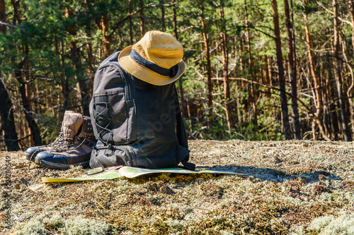 Backpack, touristic boots, map, compass and hat on a ground in a coniferous forest