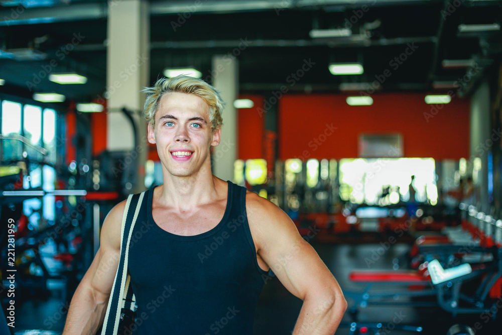 Portrait of young smiling man athlete with bag standing in gym