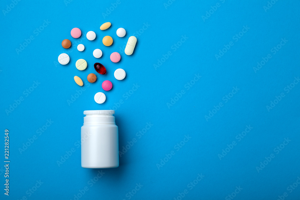 Pills spilling out of white plastic pill bottle on blue background. Top view with copy space for text, medicine drugstore concept. - obrazy, fototapety, plakaty 
