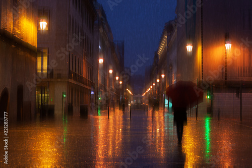 Rainy weather in the illuminated city at night. People walking under rain