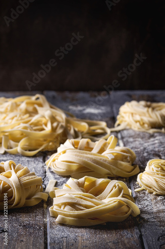 Variety of italian homemade raw uncooked pasta spaghetti and tagliatelle with semolina flour over dark plank texture wooden table. Dark rustic style