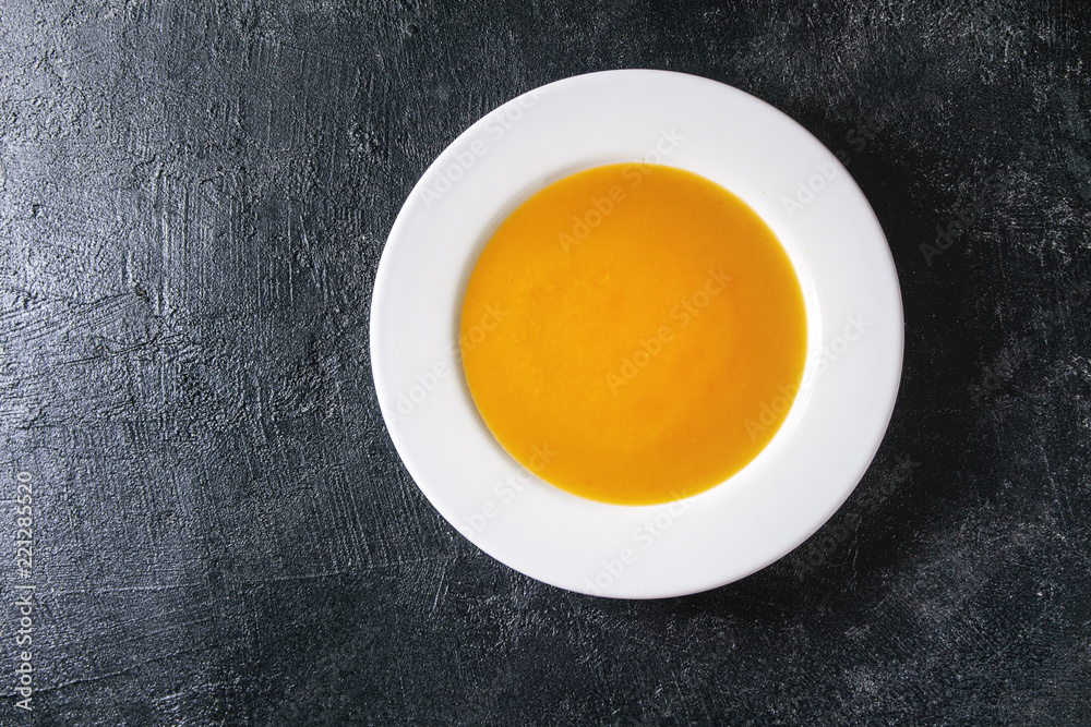Plate of vegetarian vegan pumpkin carrot soup over black texture background. Flat lay, copy space Plate of vegetarian vegan pumpkin carrot soup over black texture background. Flat lay, copy space