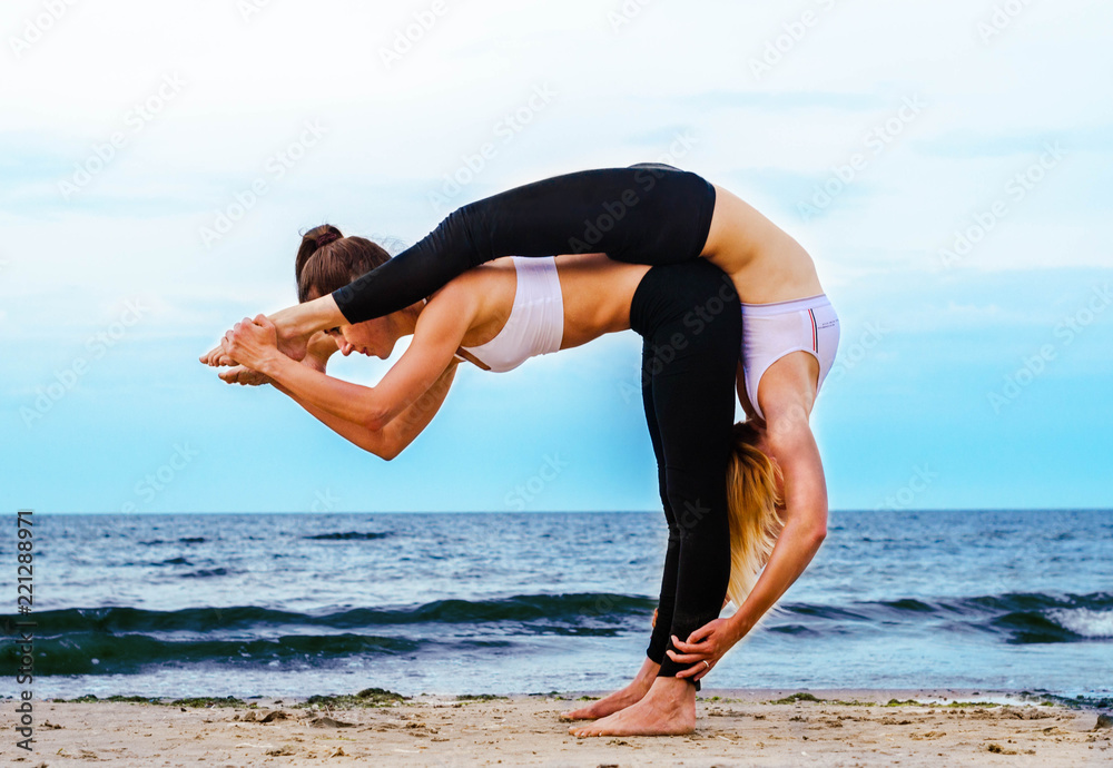 two young women on the beach in a paired acrobatic yoga pose Stock Photo