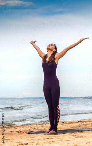 brown-haired woman performs a complex of suray namaskara on the seashore in the sand on a clear day photo