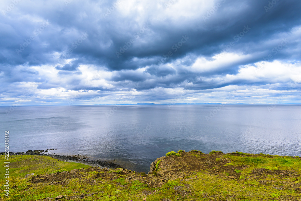 Beautiful rugged volcanic basalt rock Iceland coastline blue skies and low clouds. Green moss and grass covered hills.