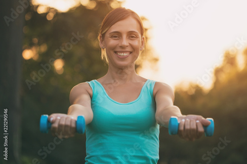 Beautiful woman enjoys exercising with weights in the nature.