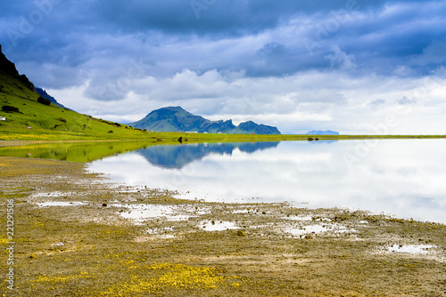 Beautiful isolated green colored Iceland lake with blue skies and puffy clouds. Reflection on water.
