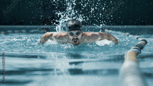 The dynamic and fit swimmer in cap breathing performing the butterfly stroke at pool. The young man. The fitsport, swimmer, pool, healthy, lifestyle, competition, training, athlete, energy concept