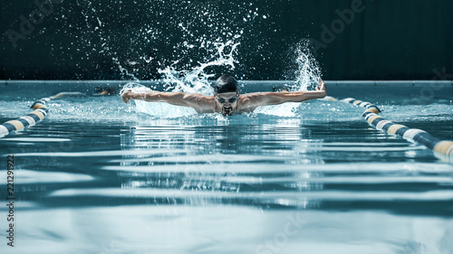 Fotografie, Obraz The dynamic and fit swimmer in cap breathing performing the butterfly stroke at pool