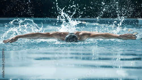 Canvas Print The dynamic and fit swimmer in cap breathing performing the butterfly stroke at pool
