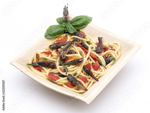 Heuschrecken gebraten auf Spaghetti mit Tomaten und Peperoni in einer Schale aus Palmblatt, nachhaltig und biologisch abbaubar. photo