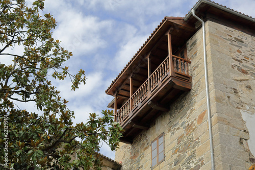 A polished wood balcony of a stone house, with a green tree and a blue sky