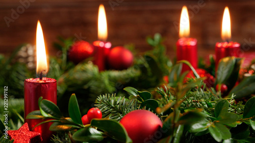Decorative advent wreath of green fir twigs and mistletoes with red candlelight and shiny baubles and stars in front of a rustic wooden wall, close-up studio shot with selective focus, nobody