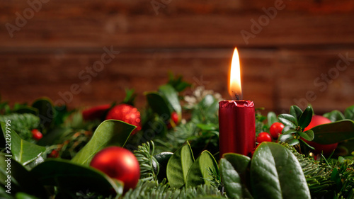 Seasonal advent wreath of green fir twigs and mistletoes with red candlelight and shiny baubles and stars in front of a rustic wooden wall, close-up studio shot with selective focus and copy space