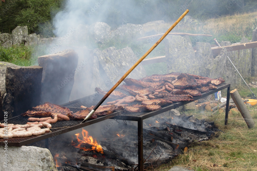 Meat being grilled and smoked on a firewood and coal bonfire during a big barbecue in Vigezzo valley, northern Italian Alps Meat being grilled and smoked on a firewood and coal bonfire during a big barbecue in Vigezzo valley, northern Italian Alps