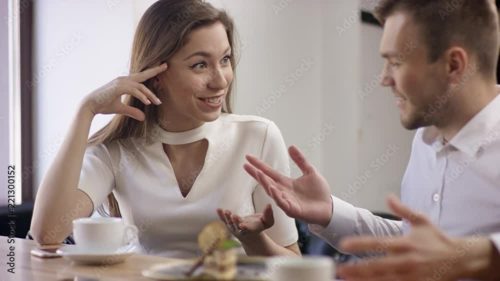 Two young people are sitting in a cafe. They are smiling and chatting. Man and woman are sitting in the restaurant at the table during break. Couple are talking and drinking coffee. Two young people are sitting in a cafe. They are smiling and chatting. Man and woman are sitting in the restaurant at the table during break. Couple are talking and drinking coffee.