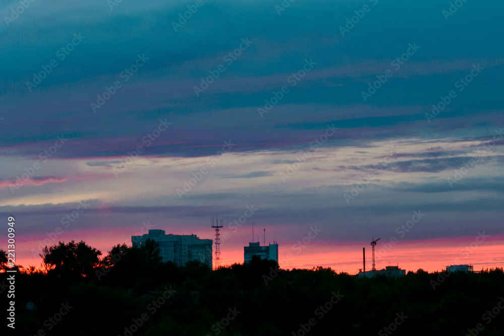 the end of a summer day: colorful sunset over line the outskirts of the city, dark sky with clouds, silhouettes of chimneys, cranes, towers and houses