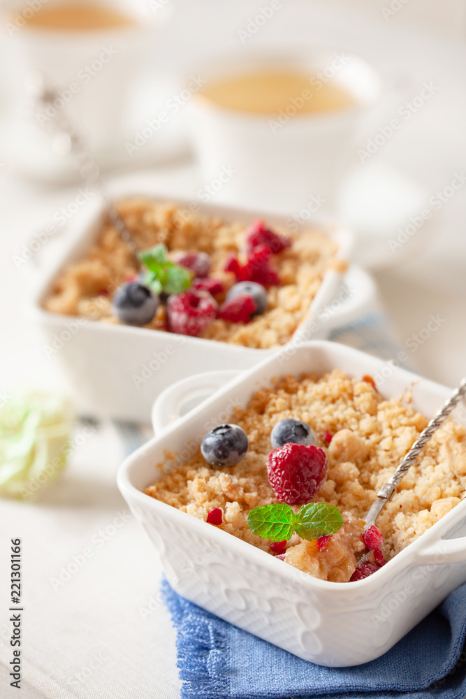 Traditional British apple crumble on portion baking dish with fresh berries Traditional British apple crumble on portion baking dish with fresh berries