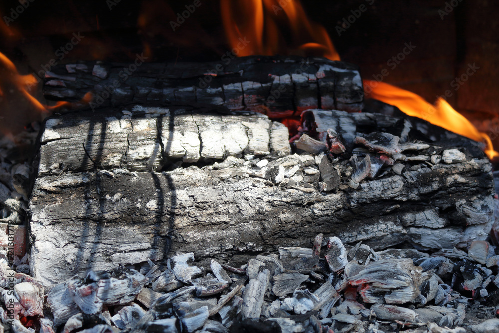 A close photo of firewood burning for a barbecue in a sunny day, with ash, carbon and flames A close photo of firewood burning for a barbecue in a sunny day, with ash, carbon and flames