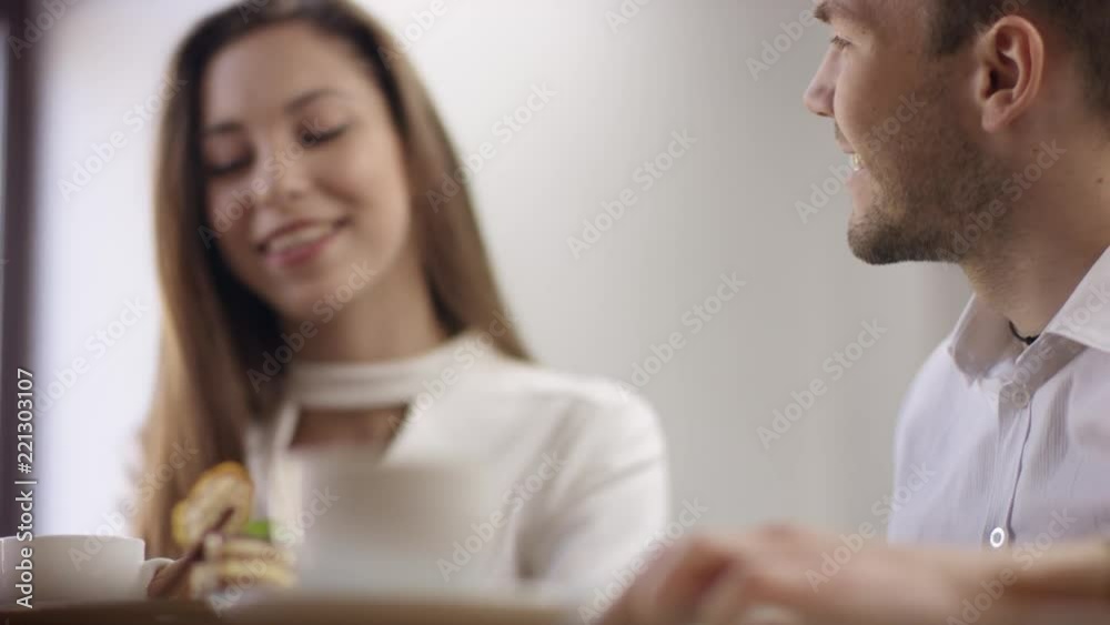Two young people are sitting in a cafe. They are smiling and chatting. Man and woman are sitting in the restaurant at the table during break. Couple are talking and drinking coffee. Two young people are sitting in a cafe. They are smiling and chatting. Man and woman are sitting in the restaurant at the table during break. Couple are talking and drinking coffee.
