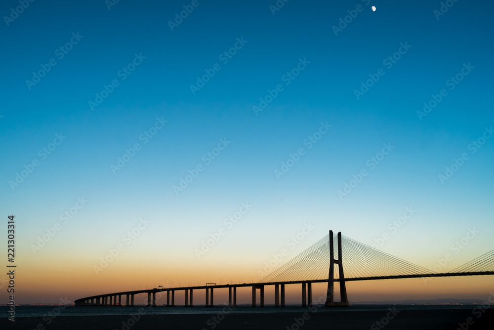 Vasco da Gama's Bridge during a sunset with clear sky and the Moon
