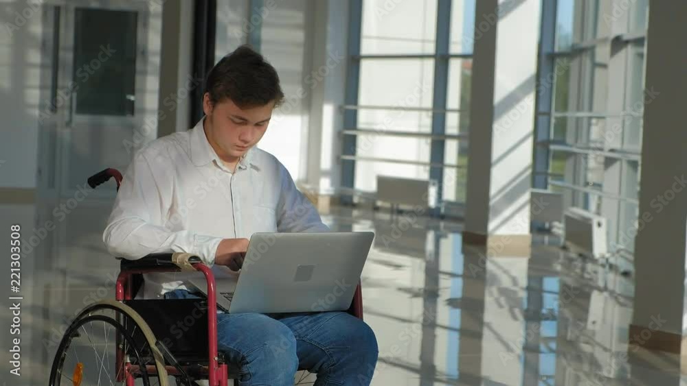 disabled businessman on a wheelchair at a window with a laptop disabled businessman on a wheelchair at a window with a laptop