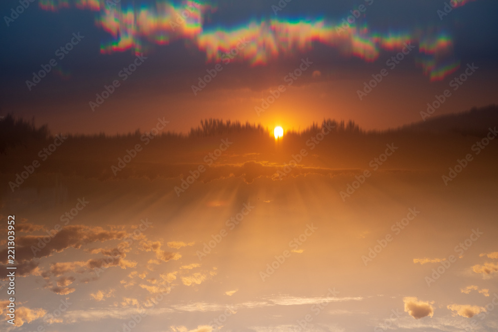 Fototapeta premium Sunset with sun almost hidden and shadows on the clouds and blue sky reflecting using a light prism
