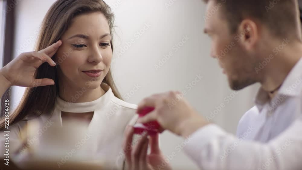 Two young people is sitting in a cafe. Man and woman are smiling and sitting in the cafe at the table during break. Couple is talking and drinking coffee. He proposes marriage Two young people is sitting in a cafe. Man and woman are smiling and sitting in the cafe at the table during break. Couple is talking and drinking coffee. He proposes marriage