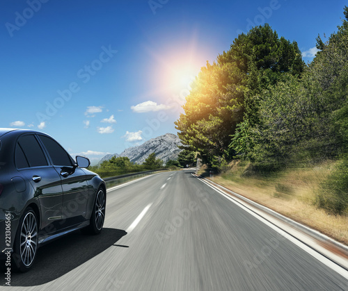 Black car rushing along a high-speed highway in the sun.