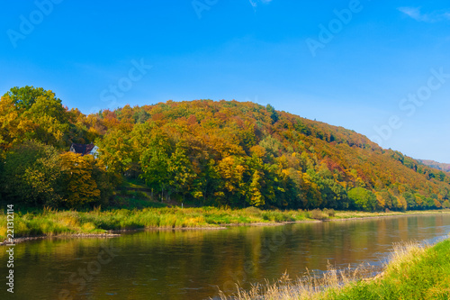 Lovely view of a riverbank in Bad Karlshafen, Germany where the river Weser runs. The weather is great, it is a sunny autumn day, the trees have colourful leaves and the sky is blue.