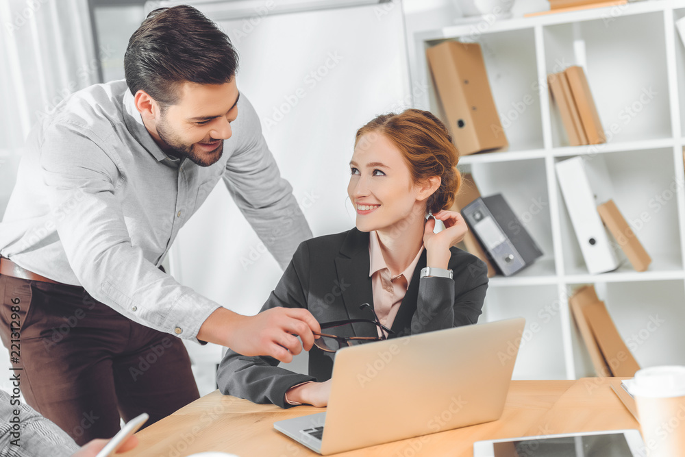 standing man in blue shirt speaking to sitting woman against laptop on table standing man in blue shirt speaking to sitting woman against laptop on table