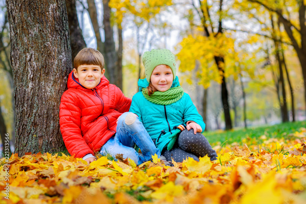 little guy with a girl sitting near a tree on the autumn foliage little guy with a girl sitting near a tree on the autumn foliage