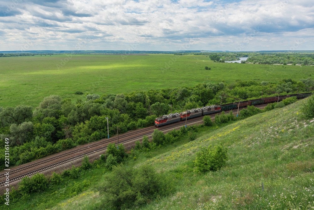 Fototapeta premium Pociąg towarowy z lokomotywami przejeżdżającymi koleją w Rosji, wzdłuż typowego rosyjskiego krajobrazu, widok z góry