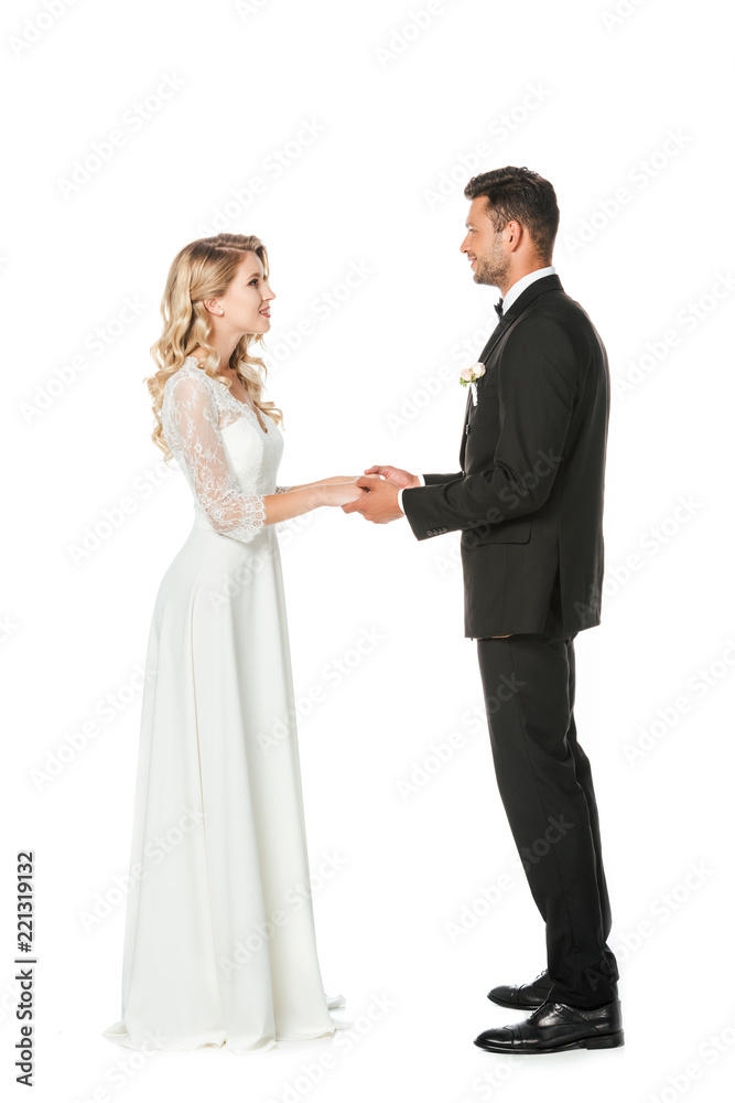 happy young bride and groom holding hands and looking at each other isolated on white happy young bride and groom holding hands and looking at each other isolated on white
