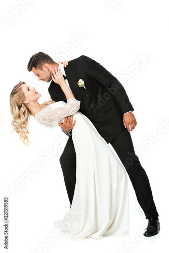 passionate young bride and groom embracing during dance and looking at each other isolated on white