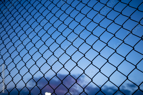 Blue sky through wire mesh fence. Blur background, close up view of link cage, wallpaper.