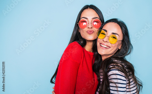 Friends forever. Two cute lovely girl friends in sunglasses posing with smile on blue background photo
