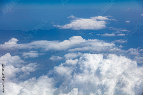 White clouds background hanging on blue sky over mountain. Aerial photo from airplane's window.